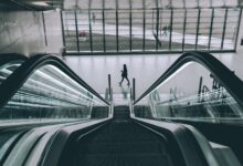 grayscale photography of person walking near escalator